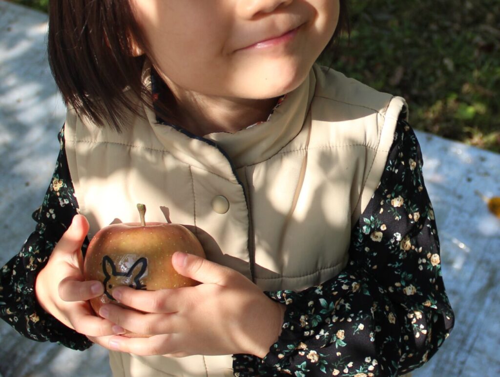 徳佐りんご園でうさぎのシールが貼られたリンゴをみつけた子供