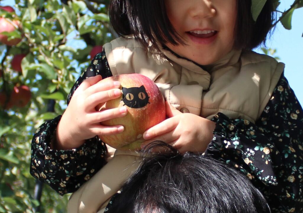 徳佐りんご園でネコのシールが貼られたリンゴをみつけた子供